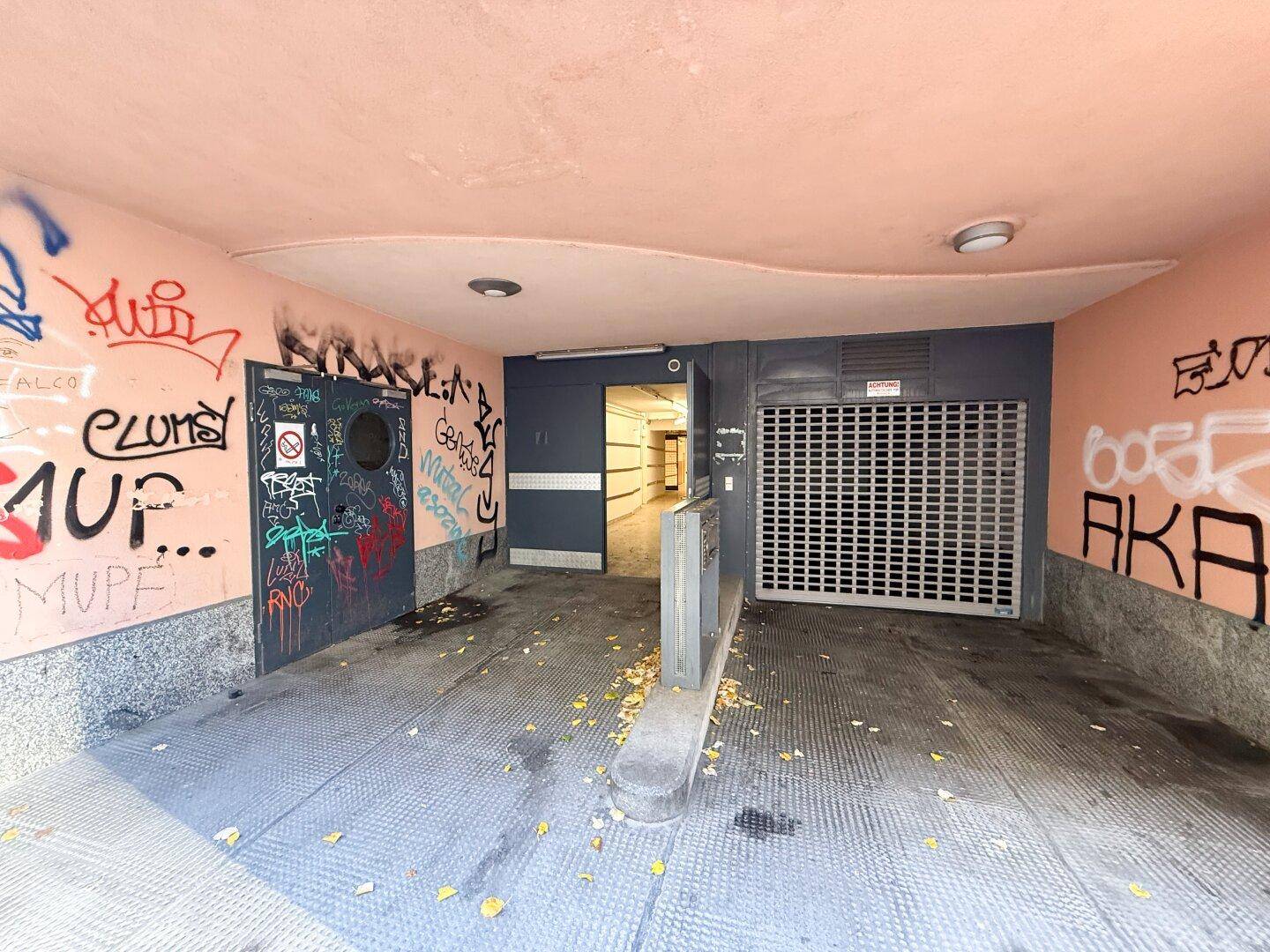 Eingangsbereich zu einer Tiefgarage mit Graffiti an den Wänden und einem geschlossenen Rolltor.