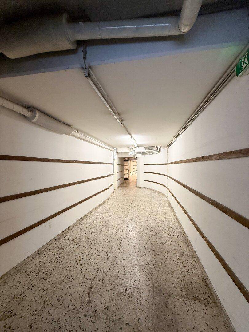 Langer, schmaler Korridor mit hellen Wänden und Terrazzoboden, der zu weiteren Räumen führt.