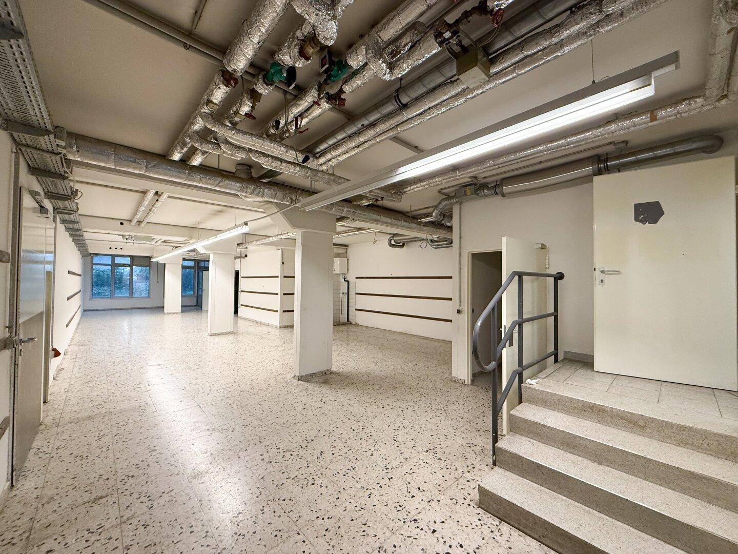 Geräumiger Kellerbereich mit Terrazzoboden, freiliegenden Rohren und einer Treppe.