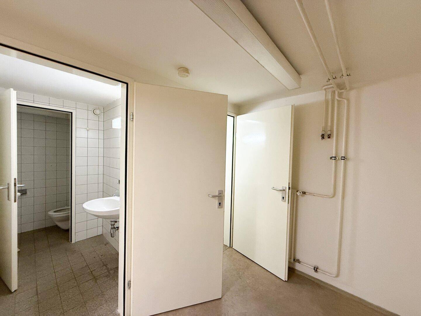 Eingang zu einem Badezimmer mit weiß gefliesten Wänden und einem sichtbaren Waschbecken.