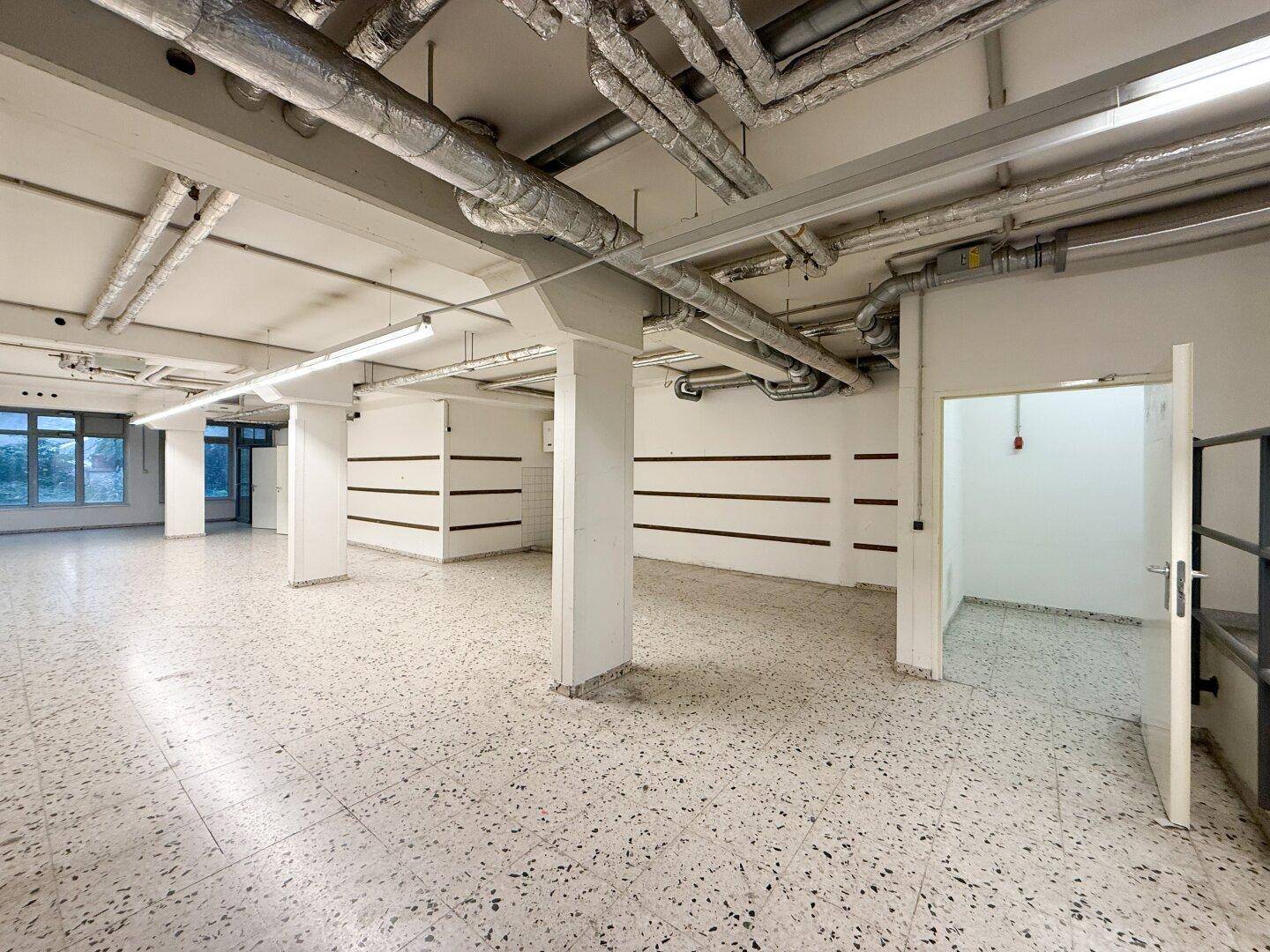 Weitläufiger Kellerbereich mit Säulen, freiliegenden Installationen und Terrazzoboden.