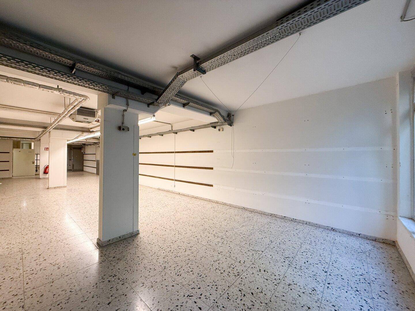 Geräumiger Kellerbereich mit Terrazzoboden, freiliegenden Kabelkanälen und Säulen.