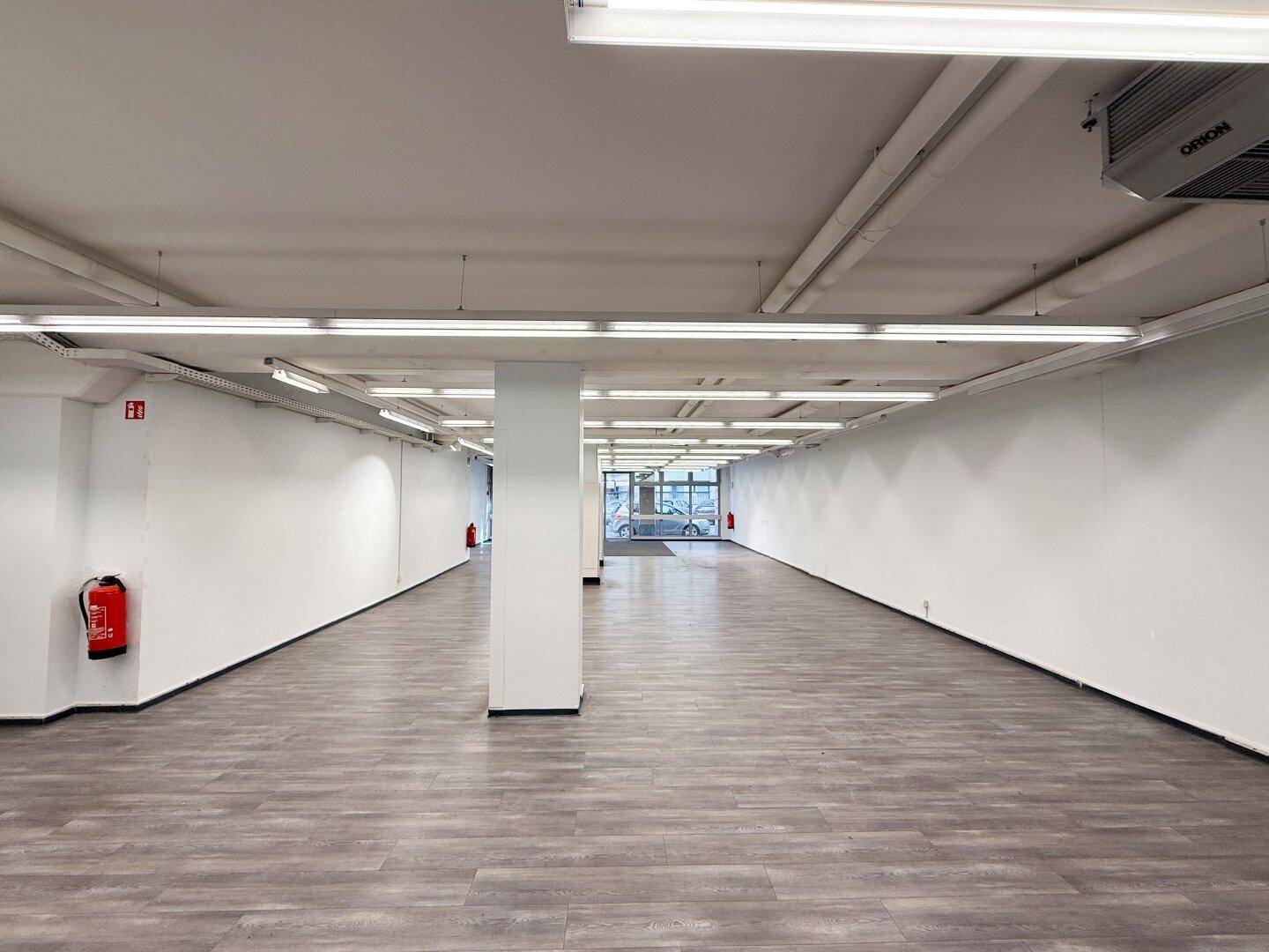 Geräumiger Gewerberaum mit modernem Laminatboden und heller Deckenbeleuchtung, bereit zur Nutzung.