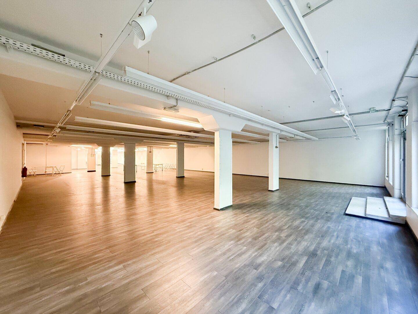 Heller, offener Gewerberaum mit vielen Säulen und Holzoptik-Laminatboden.