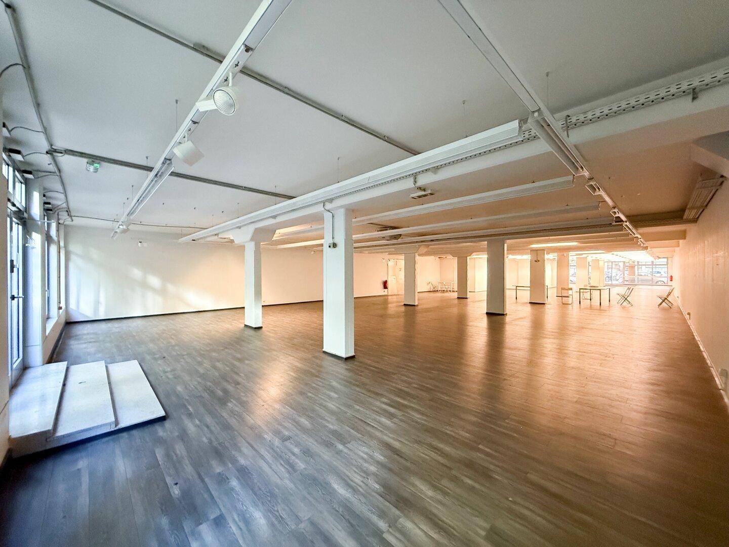 Großer Gewerberaum mit breiter Fensterfront und Holzoptik-Laminatboden.