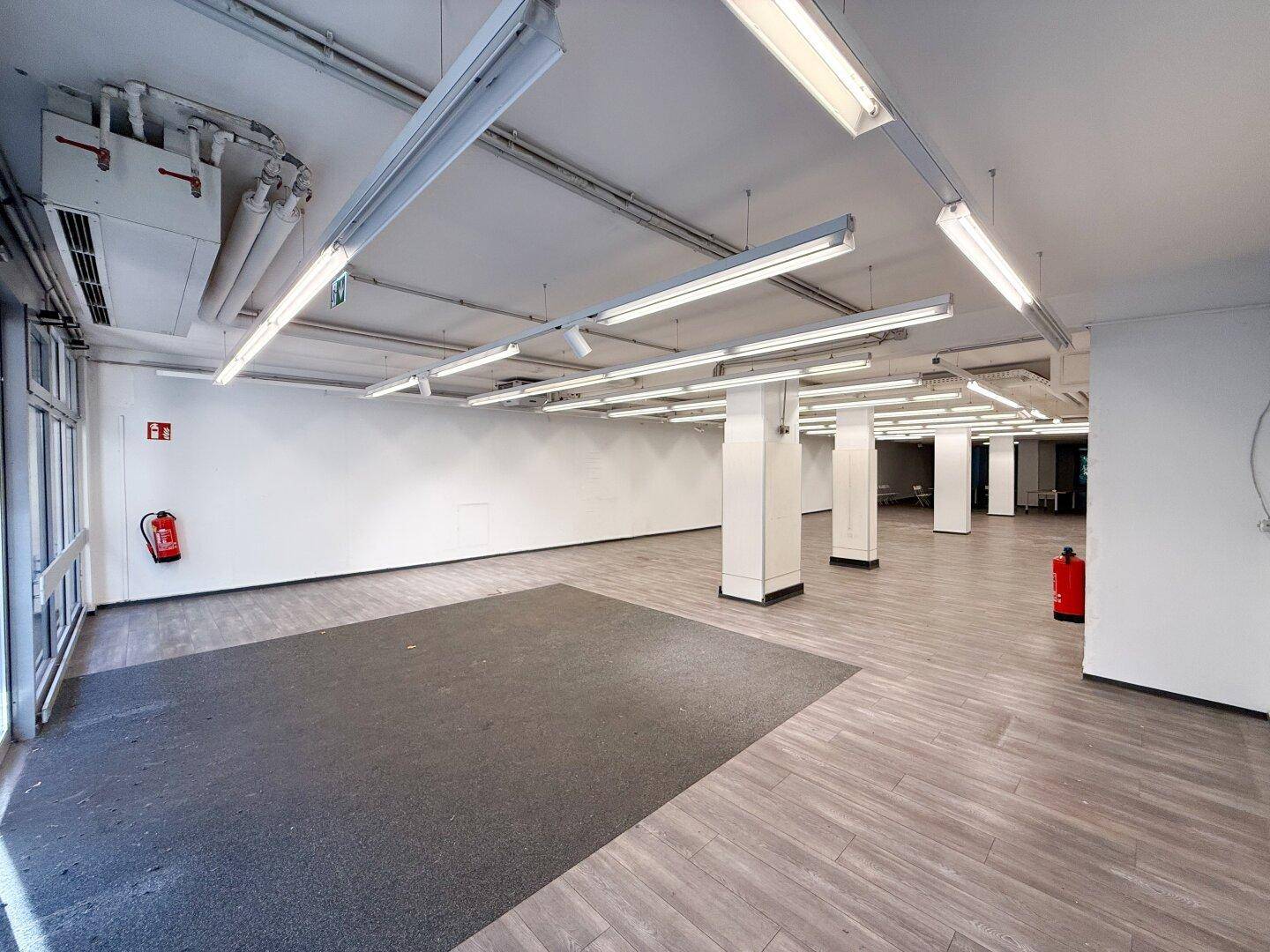 Heller Gewerberaum mit Säulen und modernem Laminatboden, ideal für verschiedene Nutzungen.