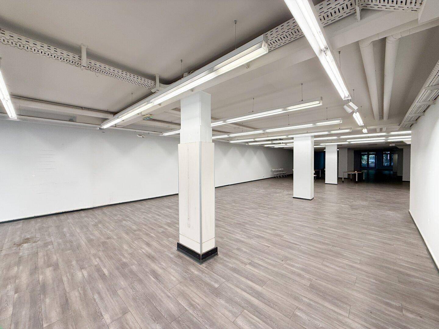 Offener Gewerberaum mit Tischen und Stühlen, viel Tageslicht und Laminatboden.