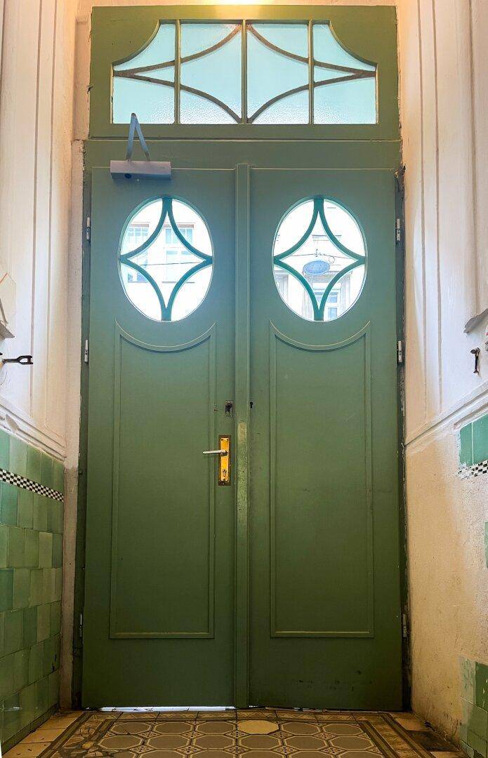 Grüne Doppeltür mit runden Glasausschnitten und einem Oberlicht im historischen Eingangsbereich.