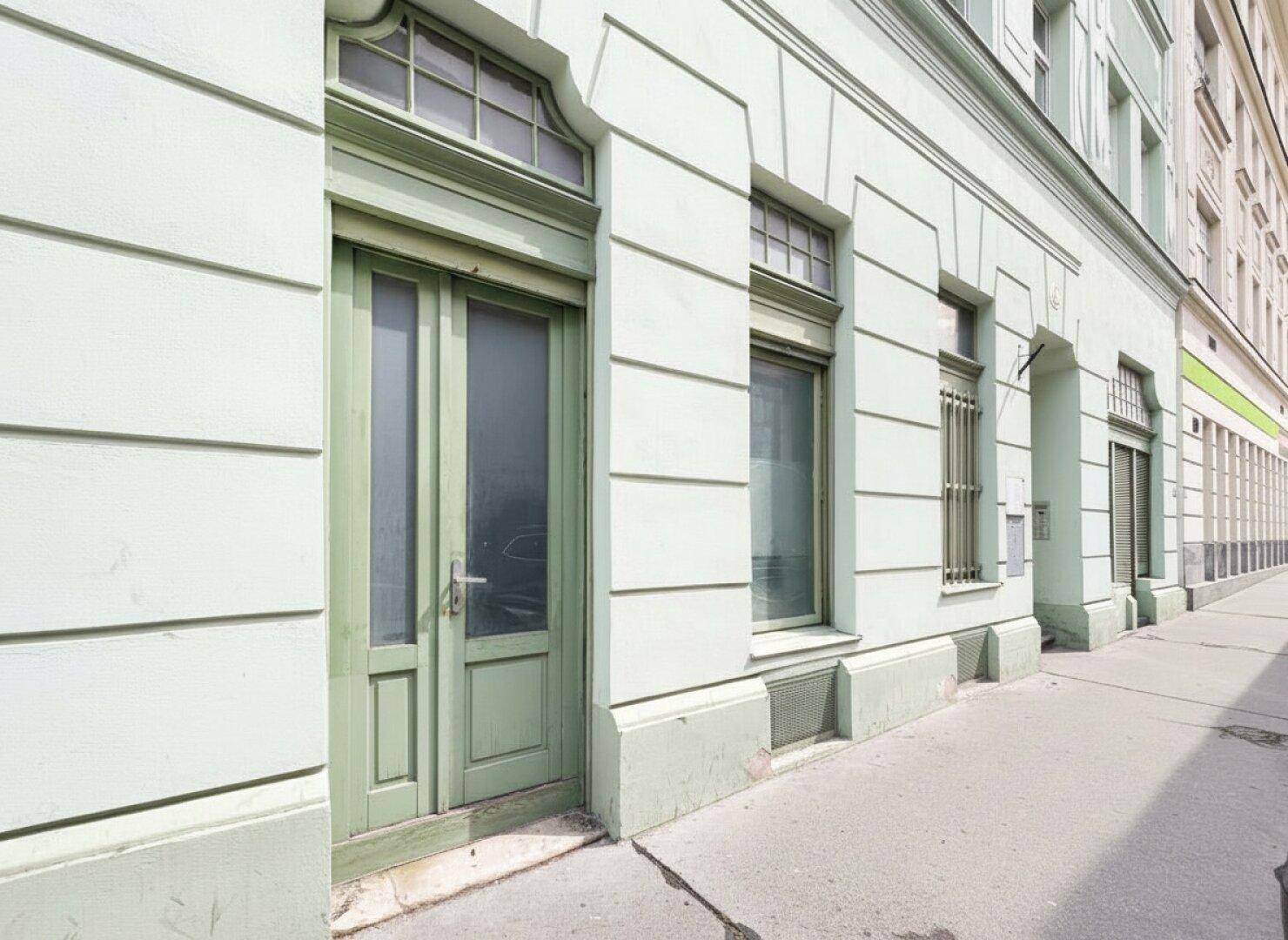 Eingangsbereich eines Gebäudes mit einer grünen Holztür und passenden Fensterrahmen an der Fassade.