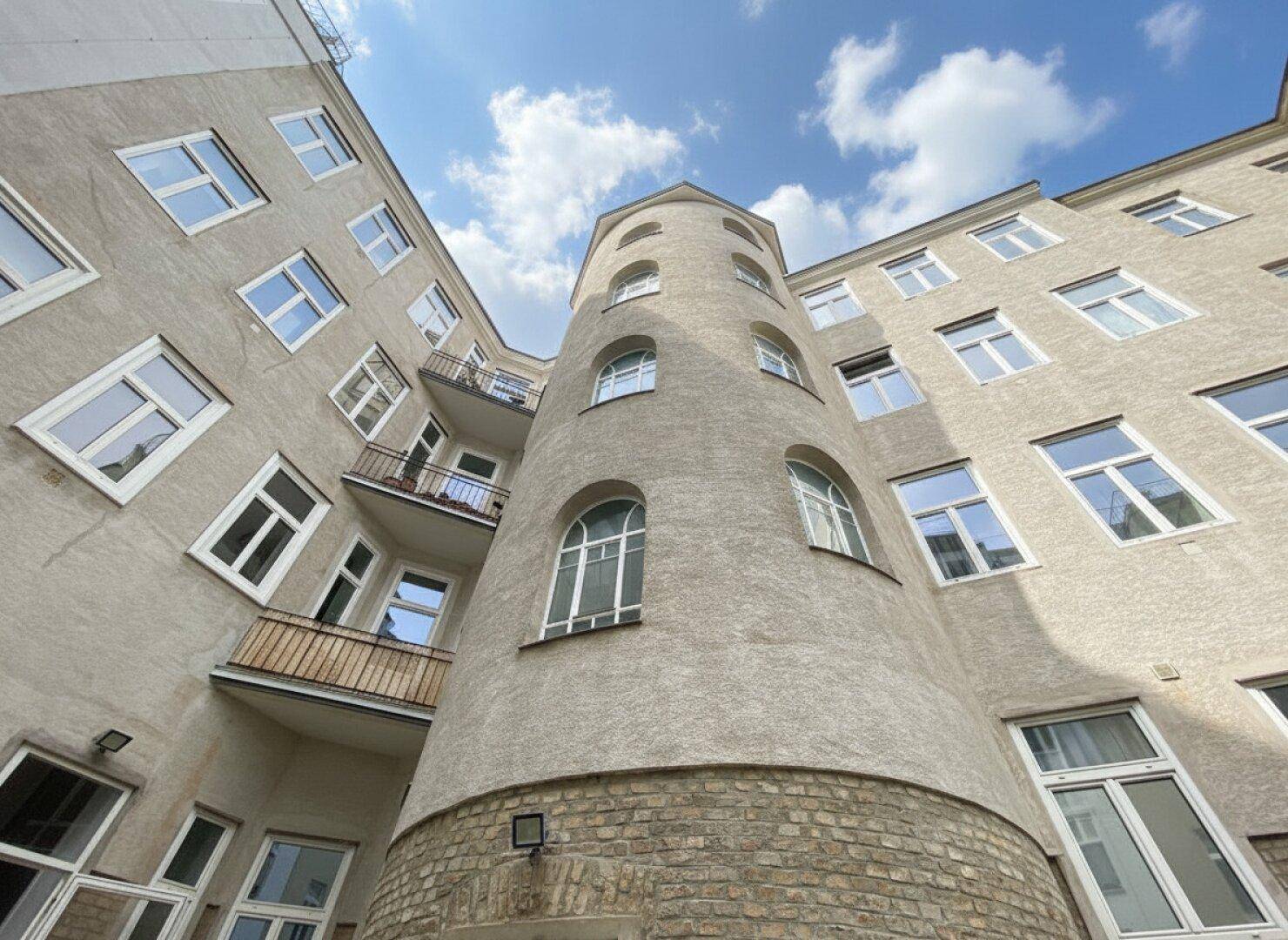 Innenhofansicht eines Gebäudes mit einem runden Turm und vielen Fenstern unter blauem Himmel.