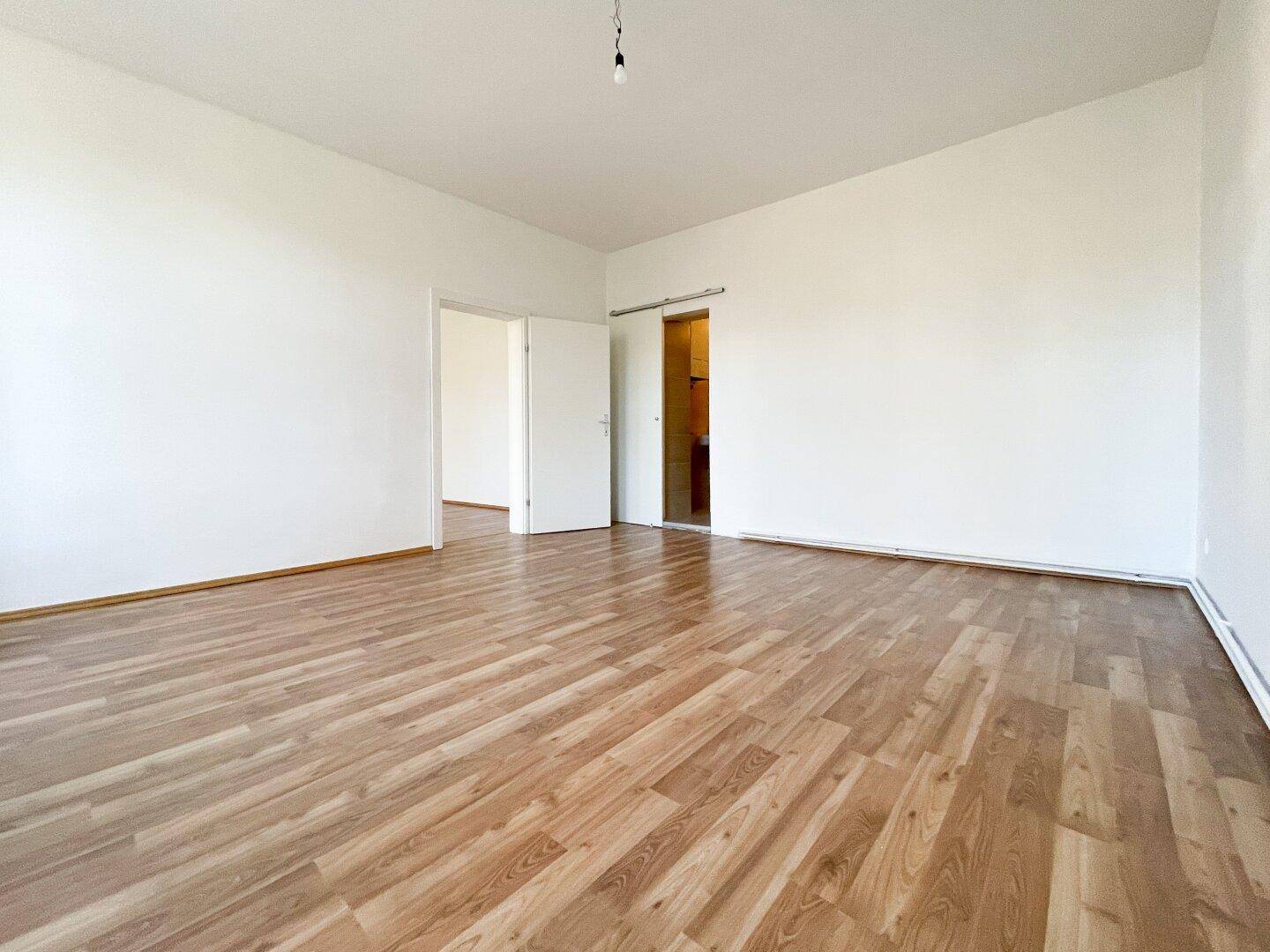 Heller Wohnraum mit Laminatboden und Zugang zu angrenzenden Zimmern, ideal für offenes Wohnen.