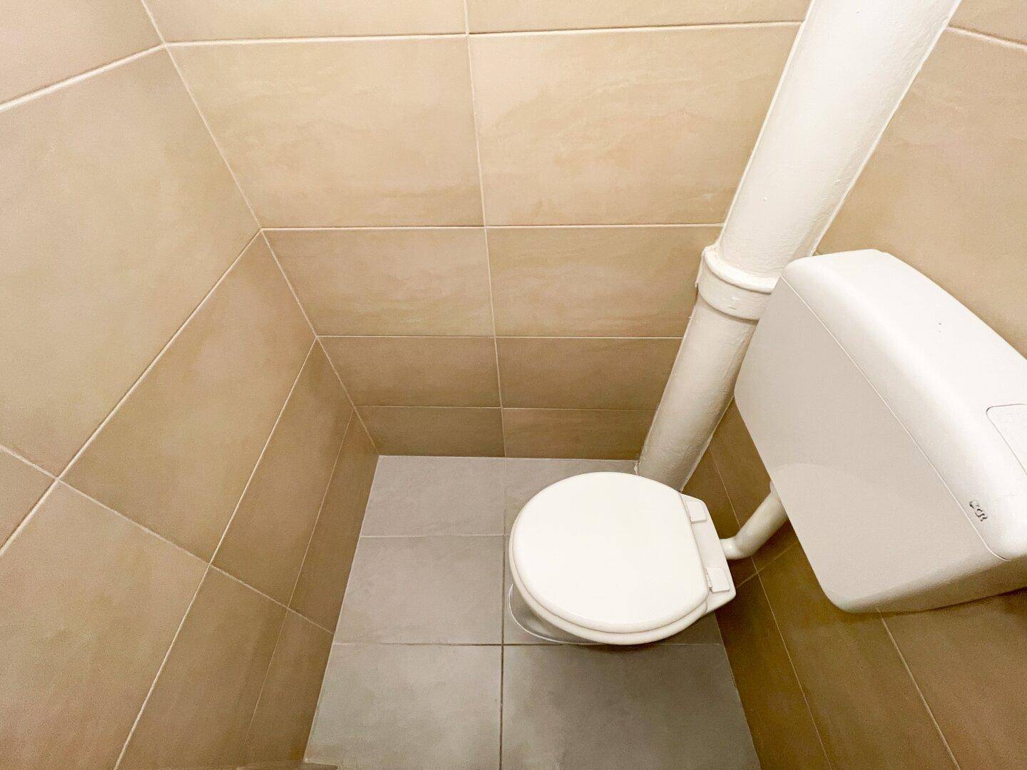 Separate Toilette mit beigefarbenen Fliesen an Wänden und Boden.