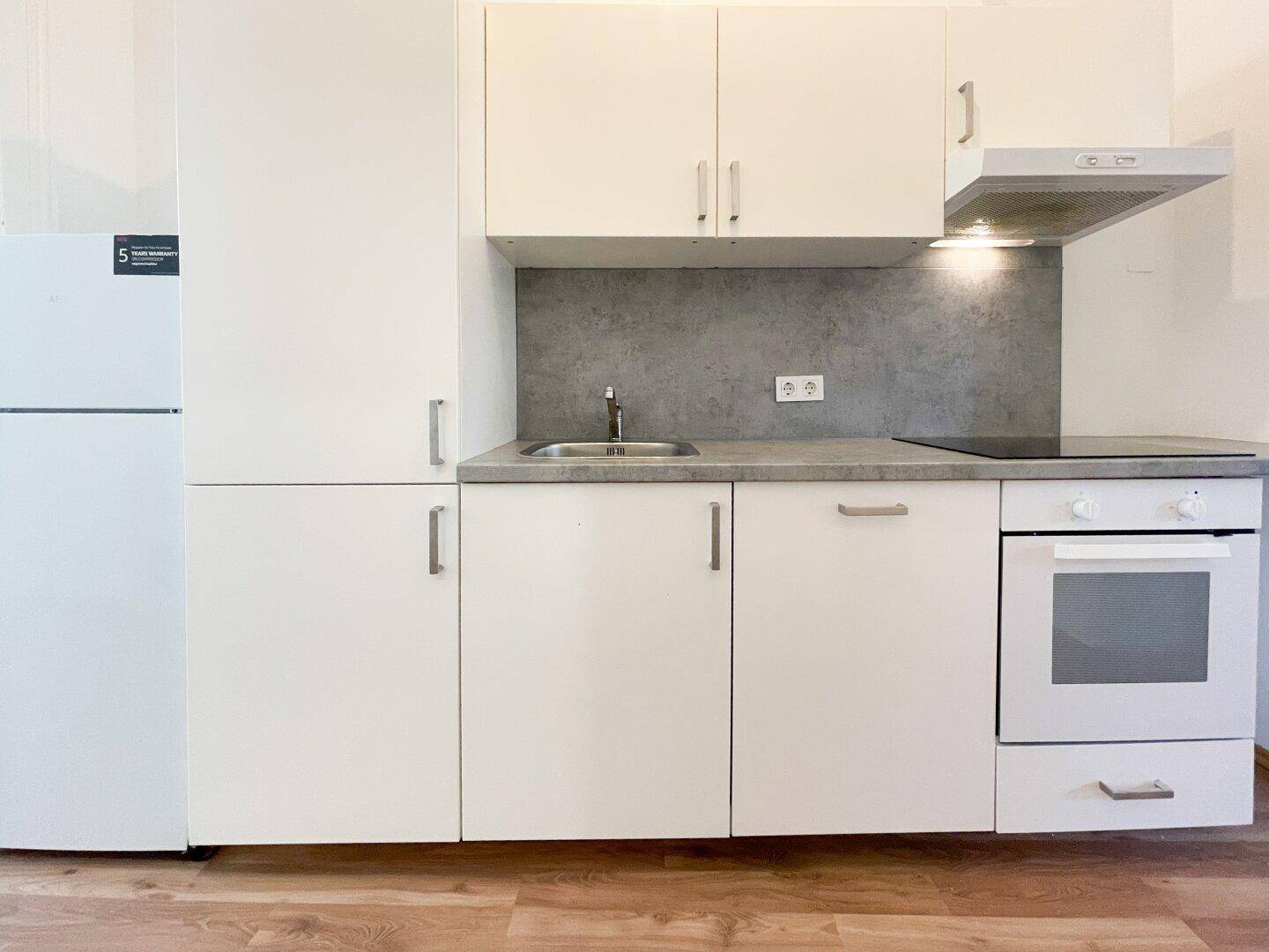 Kompakte Einbauküche mit weißen Schränken, Spüle, Herd und Kühlschrank.