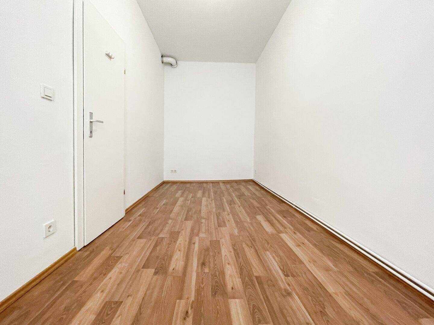 Langer, schmaler Flur mit Laminatboden und weißer Tür, verbindet verschiedene Bereiche.