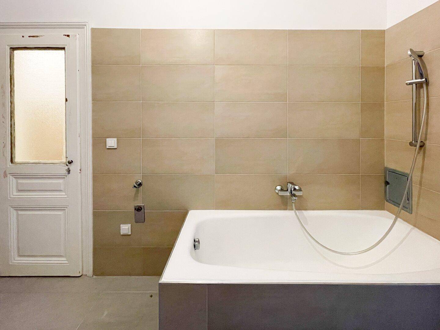 Badezimmer mit Badewanne und beigefarbenen Wandfliesen, bietet eine Duschmöglichkeit.