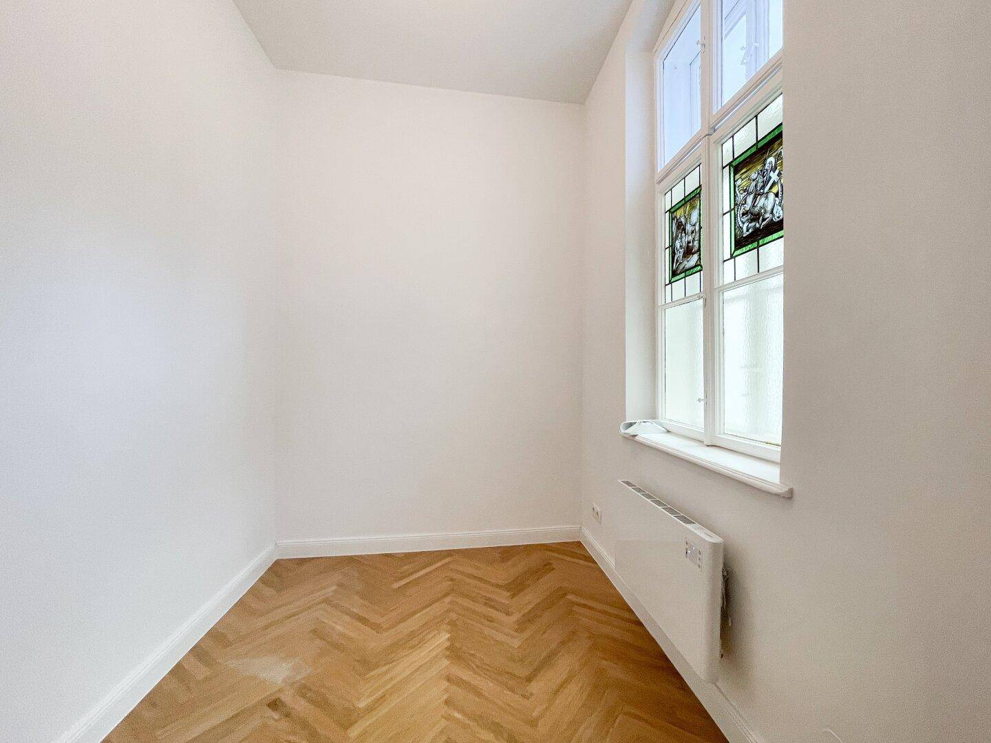 Kleines Zimmer mit Fischgrätparkett und einem einzigartigen Buntglasfenster, das für besondere Atmosphäre sorgt.