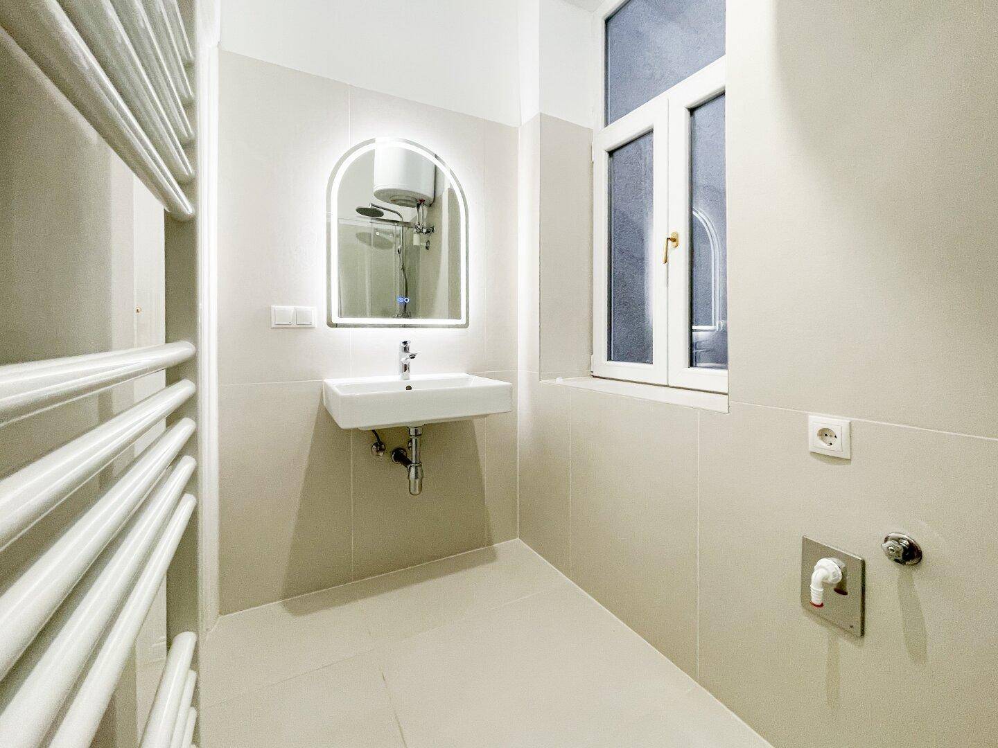 Modernes Badezimmer mit Waschbecken, beleuchtetem Spiegel und einem Fenster für natürliches Licht.
