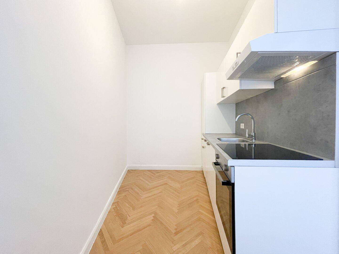 Funktionale Küchenzeile mit weißen Schränken, integrierten Geräten und einem Fenster für Tageslicht.