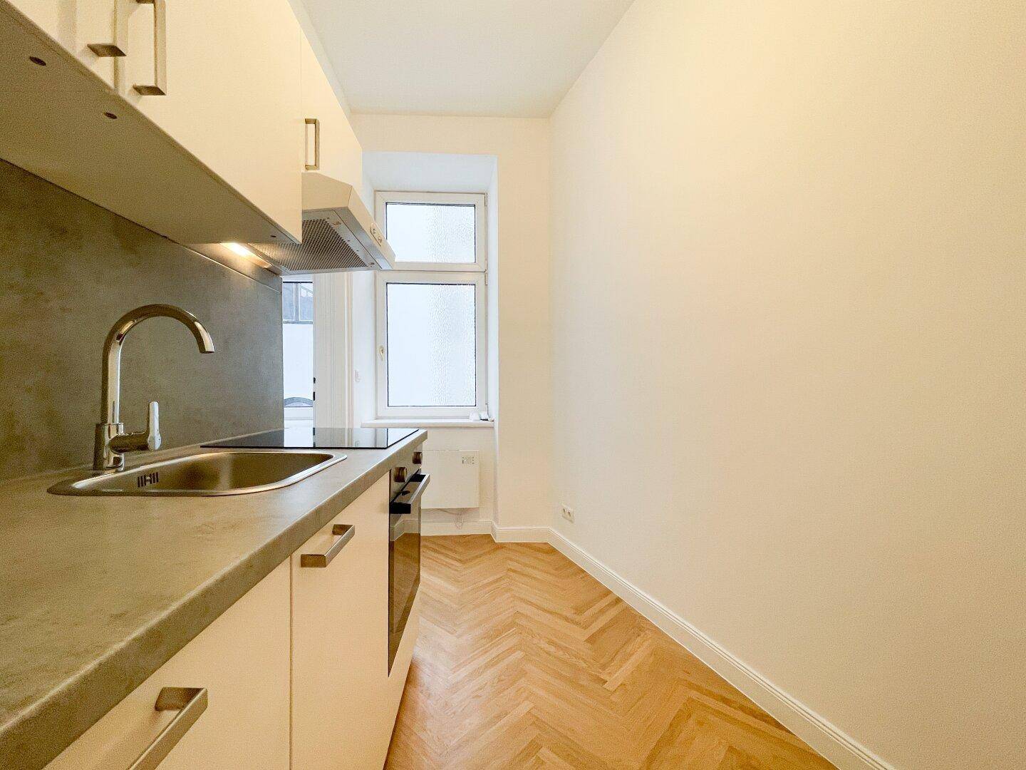Helle Küchenzeile mit Fenster, weißen Fronten und moderner Ausstattung, ideal für kleine Wohnungen.