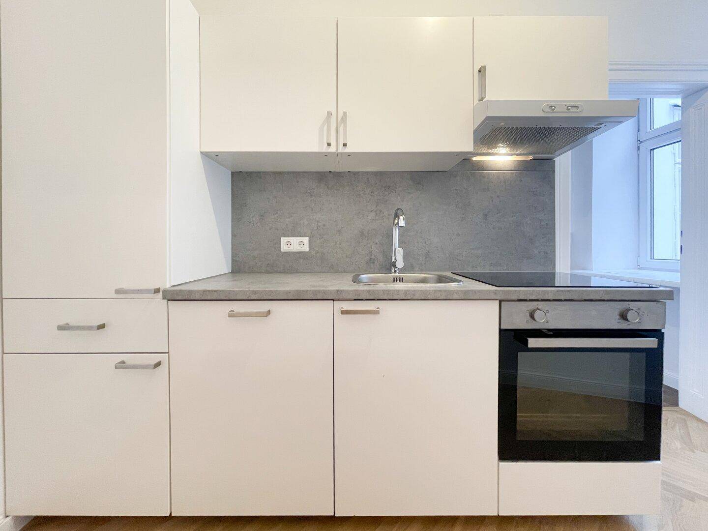 Moderne, kompakte Küchenzeile mit weißen Schränken, integriertem Backofen und Kochfeld.