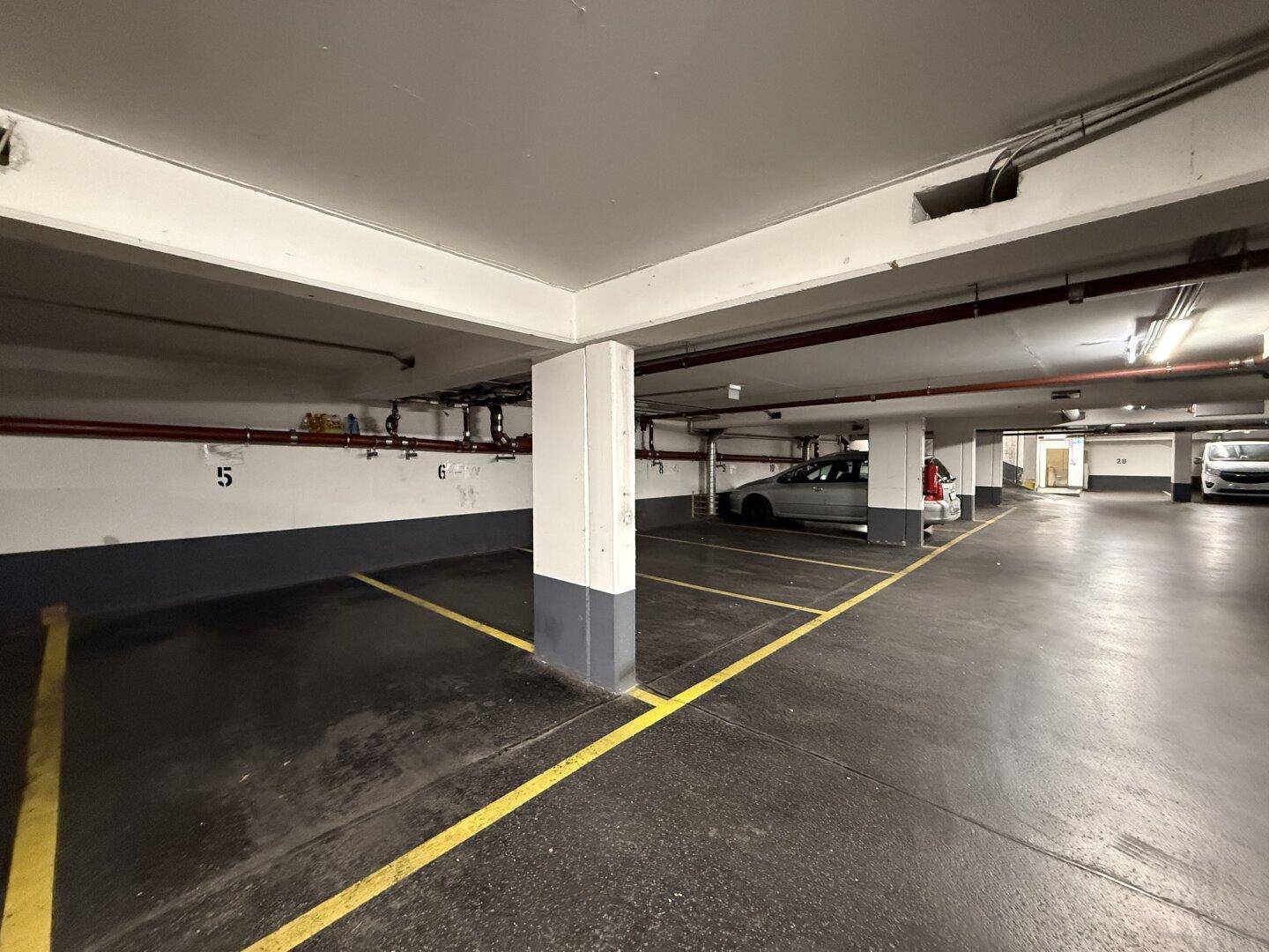 Tiefgarage mit markierten Stellplätzen und einem geparkten Fahrzeug, gut beleuchtet.
