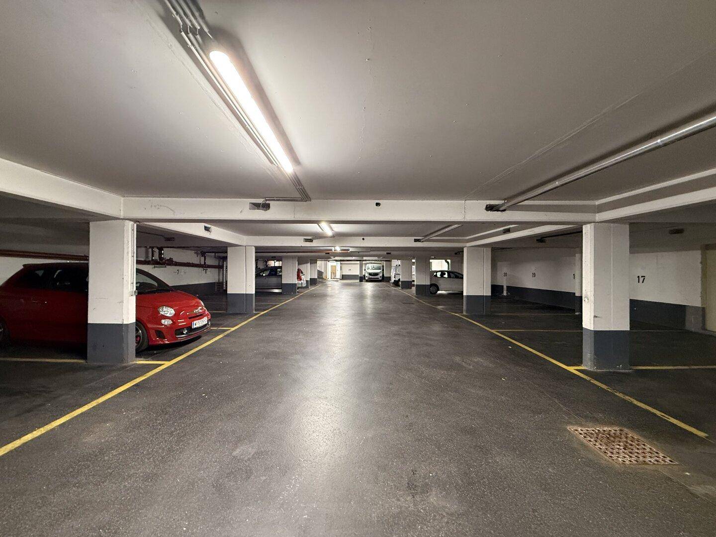 Langer Gang in der Tiefgarage mit parkenden Autos auf beiden Seiten und heller Beleuchtung.