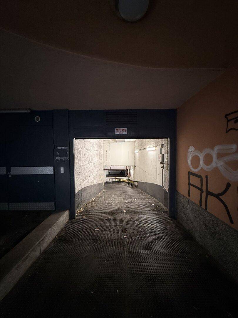 Einfahrt zur Tiefgarage mit einer Rampe, die in das Gebäude führt, bei schlechten Lichtverhältnissen.
