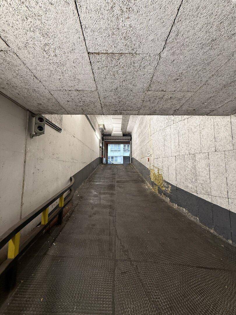Die Zufahrtsrampe zur Tiefgarage mit strukturiertem Boden und Blick auf den Ausgang.