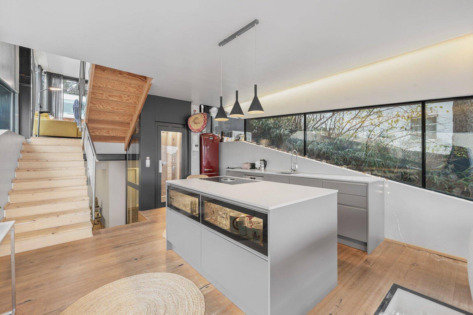 Stilvolle offene Küche mit Kochinsel, rotem Kühlschrank und Zugang zur Holztreppe.