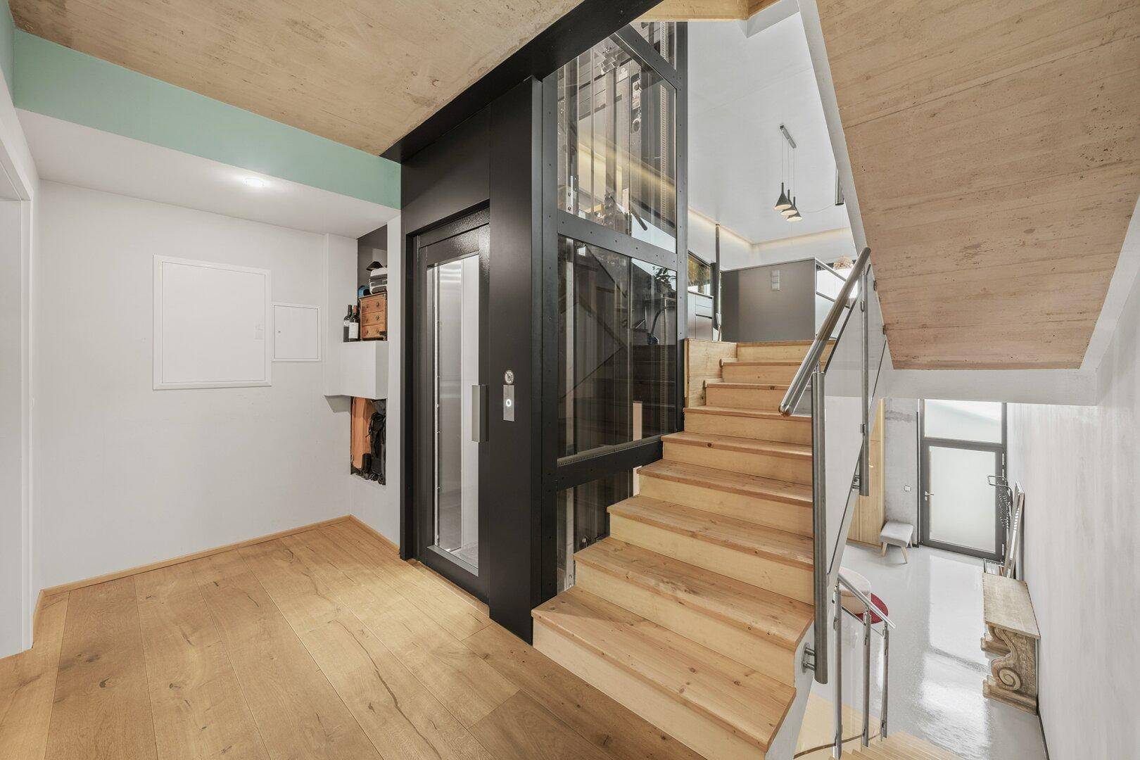Elegantes Treppenhaus mit Holzstufen und einem modernen Glasaufzug.