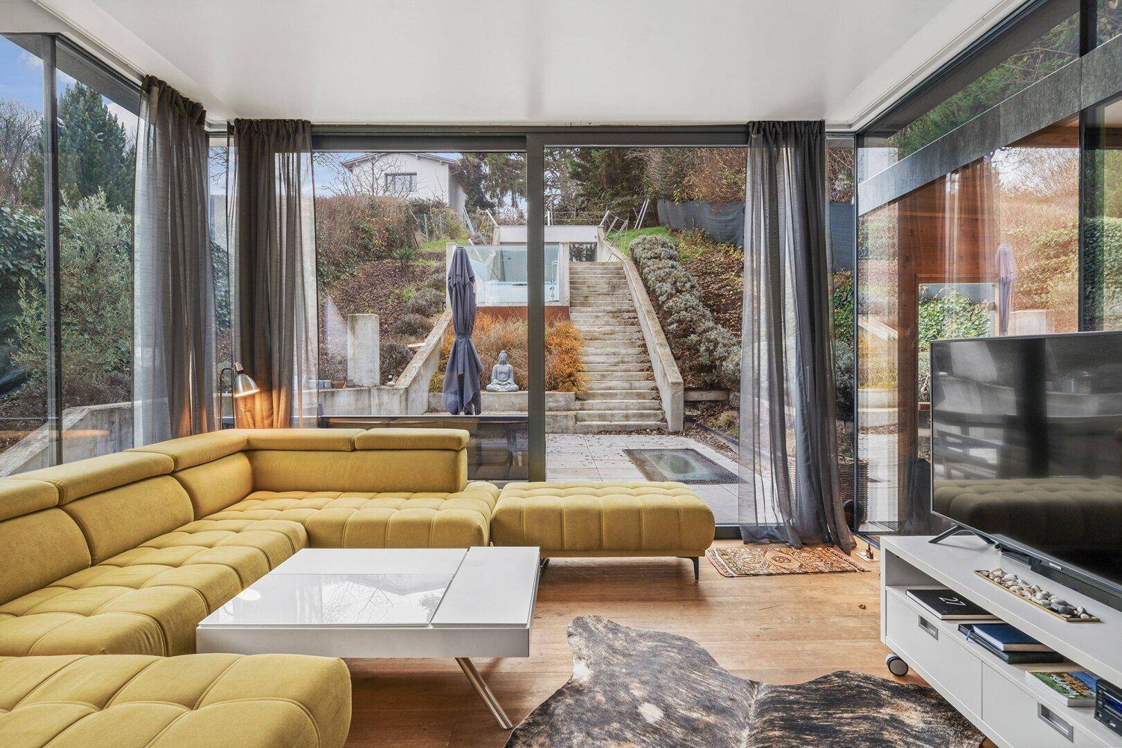 Lichtdurchflutetes Wohnzimmer mit großem Sofa und direktem Blick auf den terrassierten Garten.