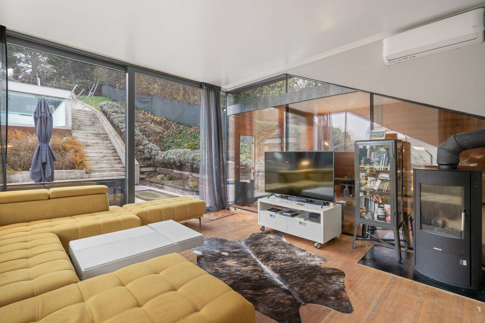 Gemütliches Wohnzimmer mit gelbem Sofa, Kamin und bodentiefen Fenstern zum Garten.