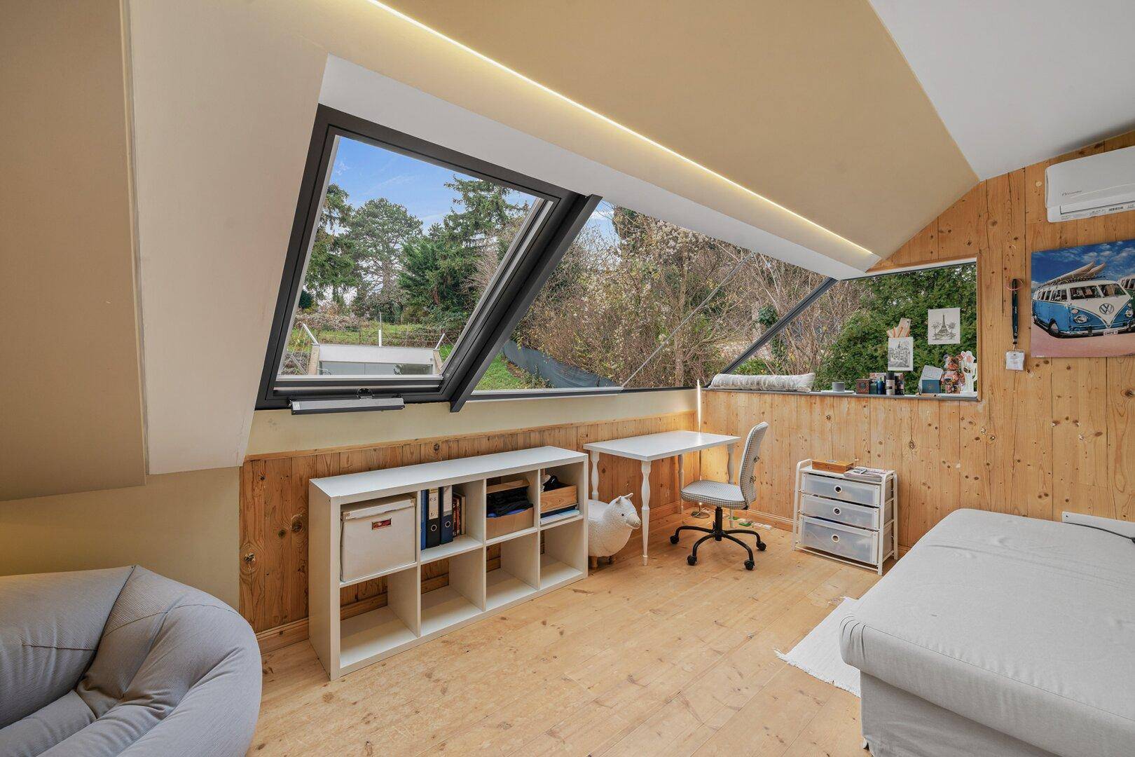Helles Zimmer mit Dachschräge, Holzvertäfelung und großem Fenster mit Blick ins Grüne.