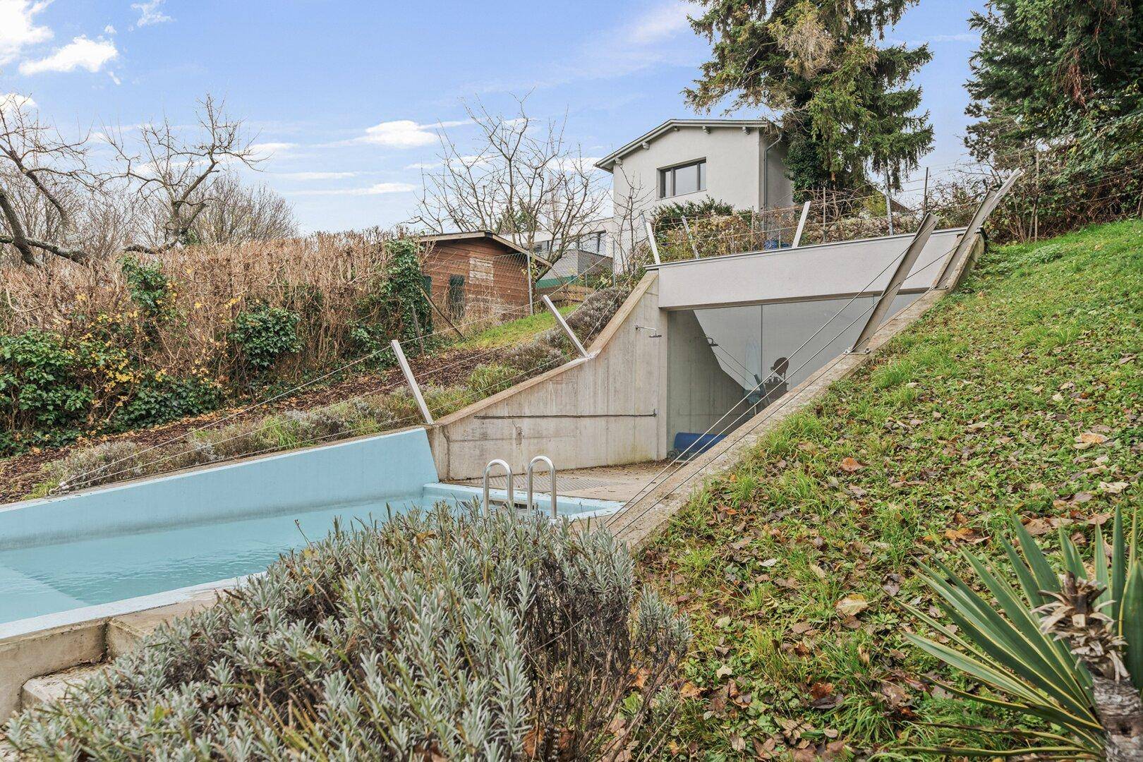 Außenbereich mit Pool und Garageneinfahrt, eingebettet in eine grüne Hanglage.