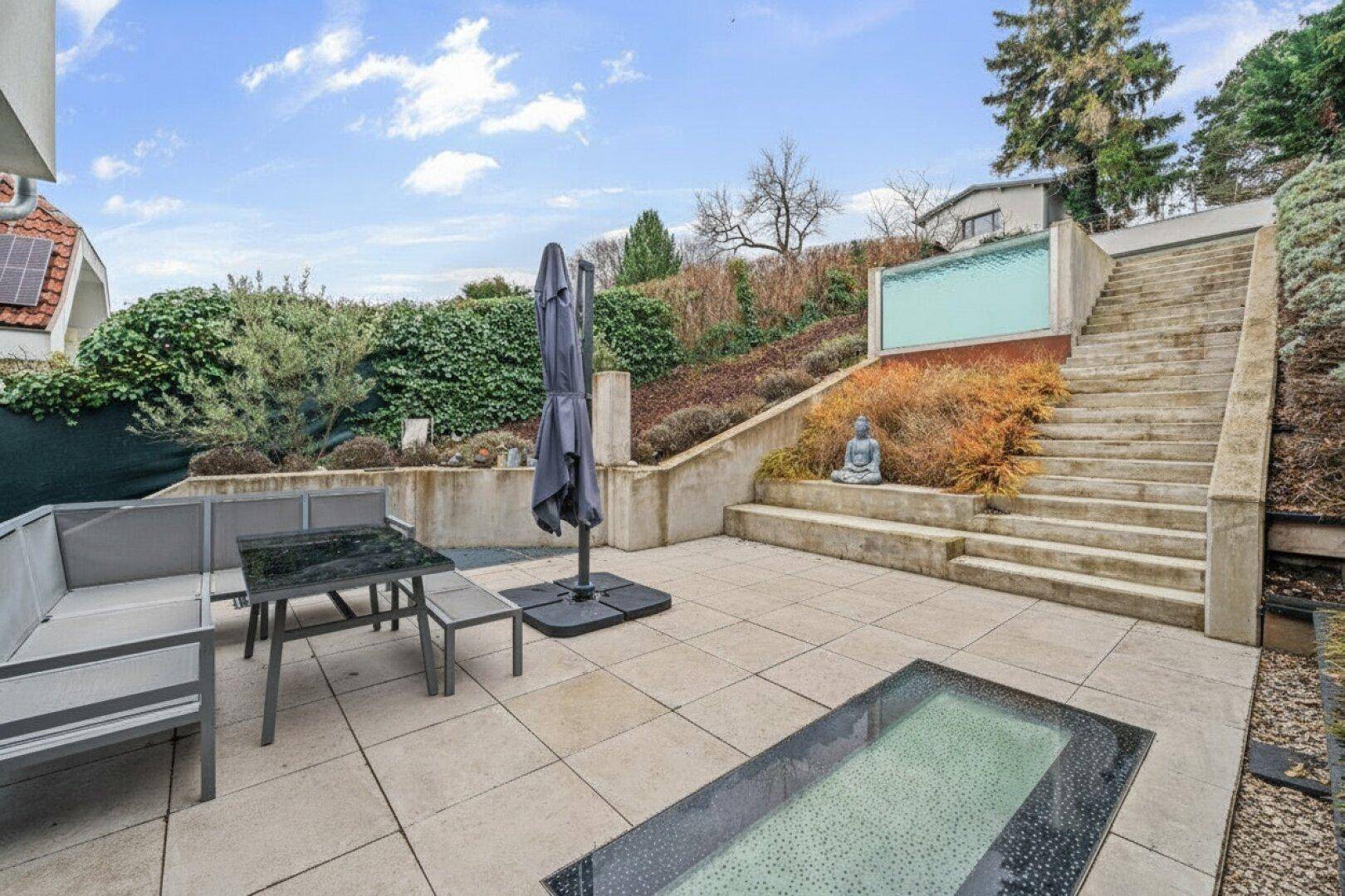 Geräumige Terrasse mit modernen Sitzmöbeln und Treppen, die zum terrassierten Garten führen.