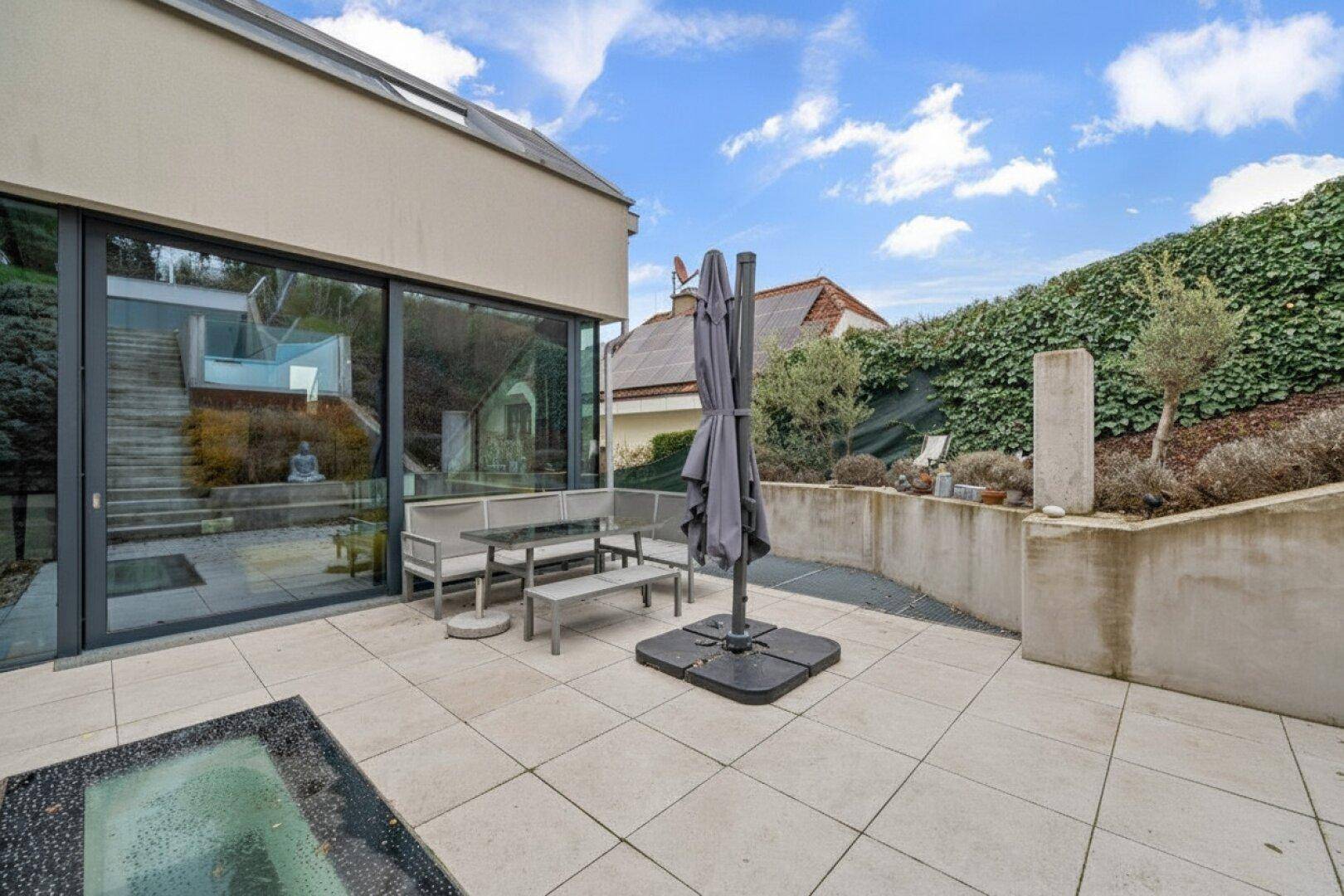 Große gepflasterte Terrasse mit Sitzgelegenheiten und Zugang zum Garten.