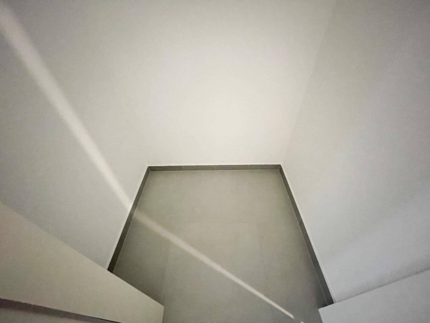 Weiße Decke mit minimalistischem Design und natürlichen Lichtstrahlen, die den Raum erhellen.