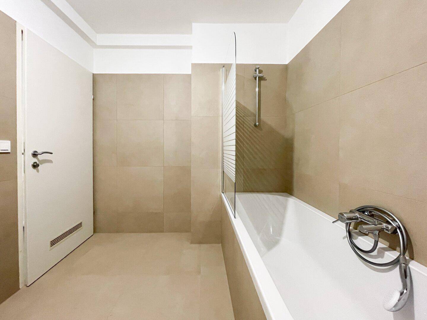 Badezimmer mit Badewanne, Duschabtrennung und beigefarbenen Wand- und Bodenfliesen.