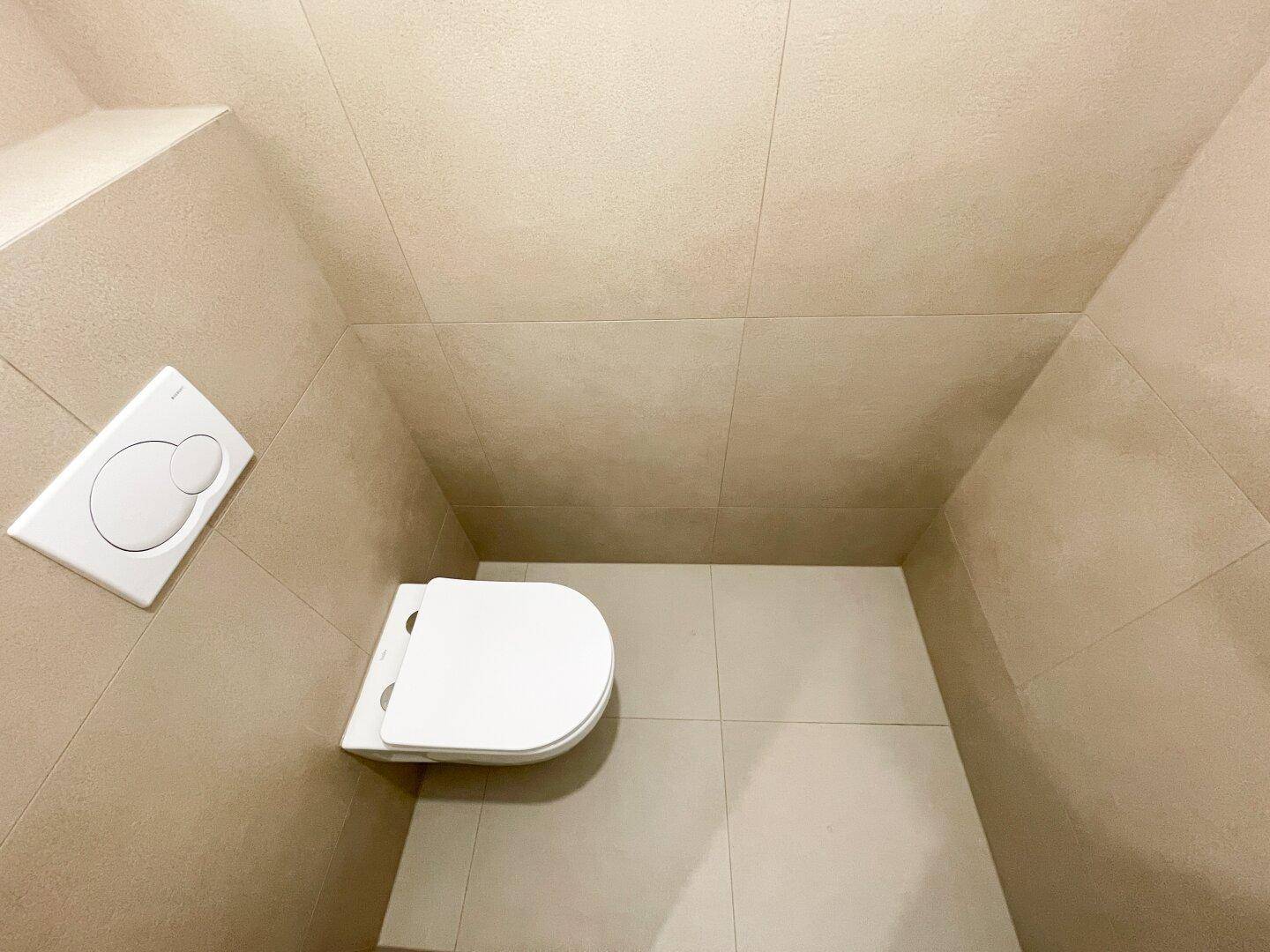 Kleine Gästetoilette mit Wand-WC und beigefarbenen Fliesen an Wänden und Boden.