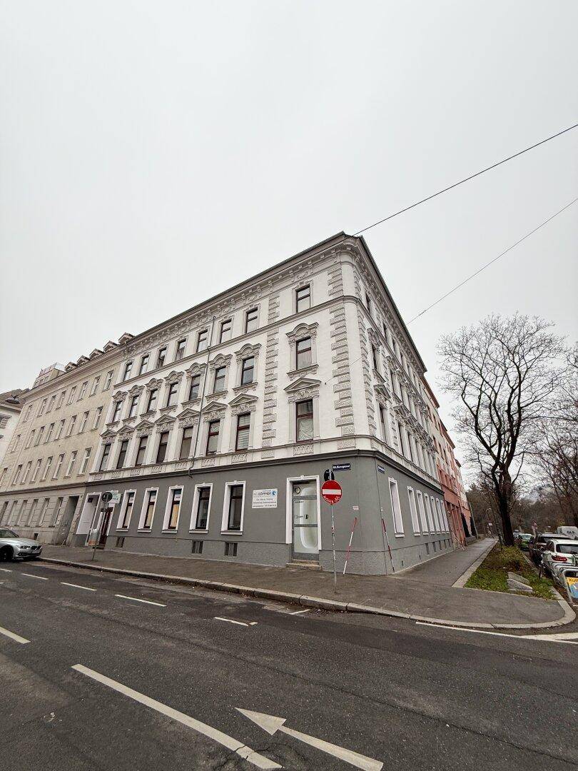 Eckgebäude mit klassischer Architektur und Geschäften im Erdgeschoss an einer Straße.