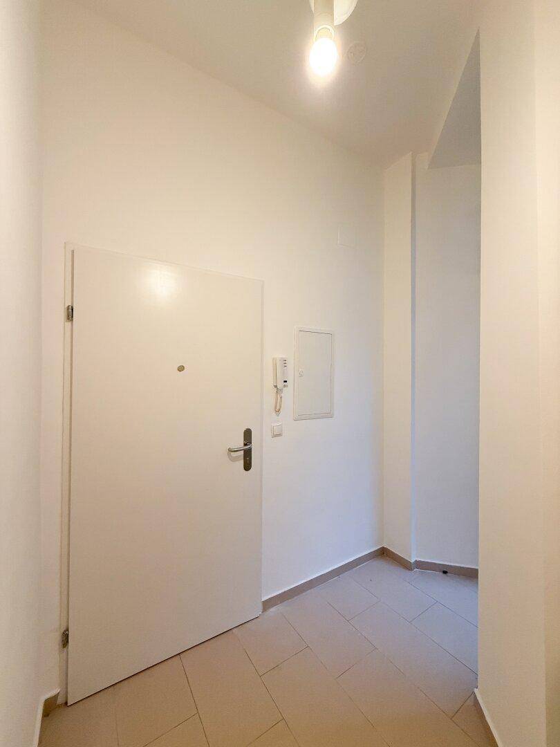 Heller Eingangsbereich mit weißer Wohnungstür, Gegensprechanlage und Fliesenboden.