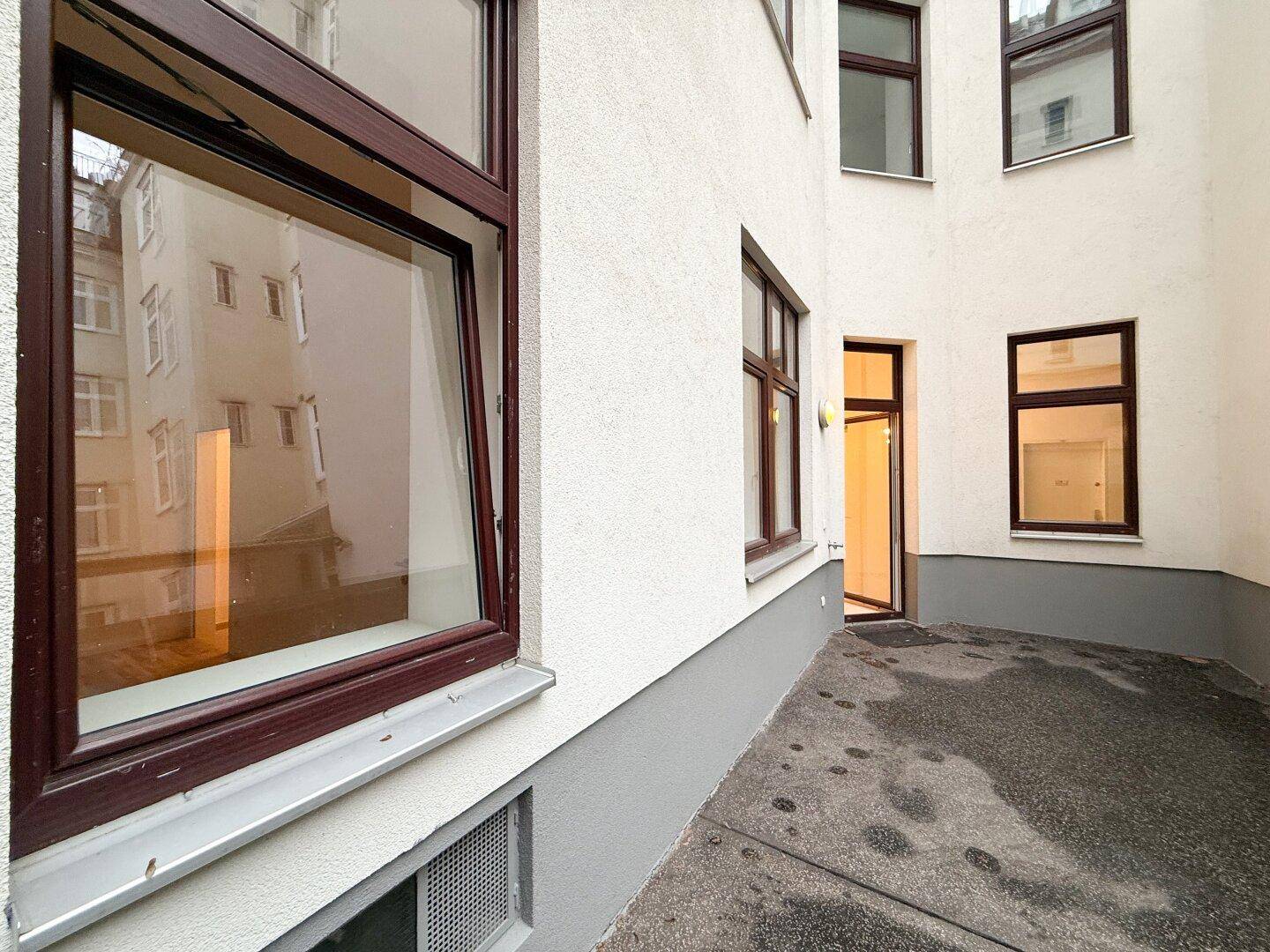 Detailansicht der Gebäudefassade mit Fenstern und dem gepflasterten Innenhofbereich.