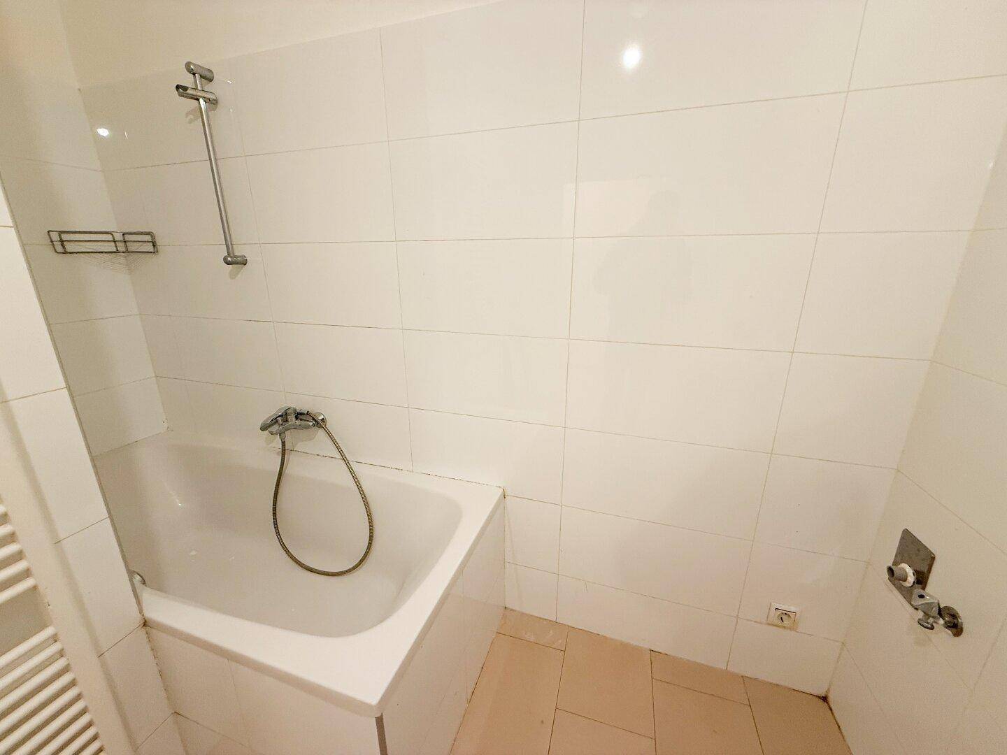 Nahaufnahme der Badewanne mit Duscharmatur und weißen Wandfliesen.