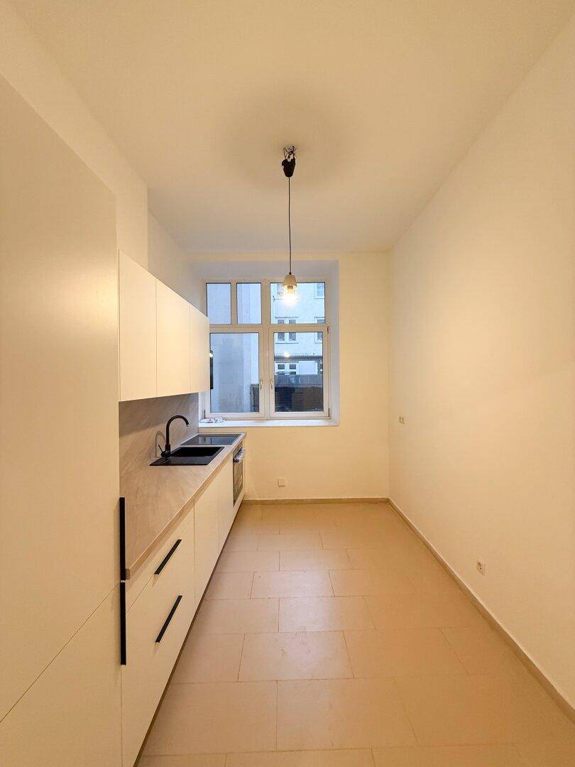 Moderne Küche mit neuen weißen Schränken, schwarzer Spüle und einem Fenster.