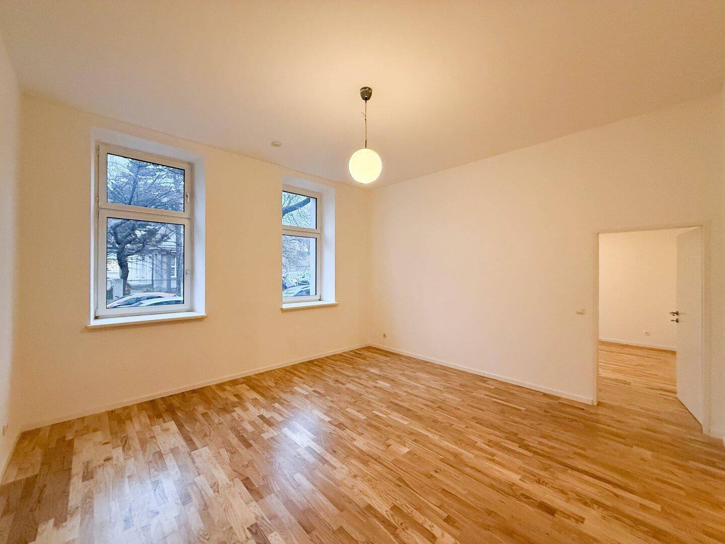 Geräumiges Wohnzimmer mit Holzboden und Blick auf den Eingangsbereich.