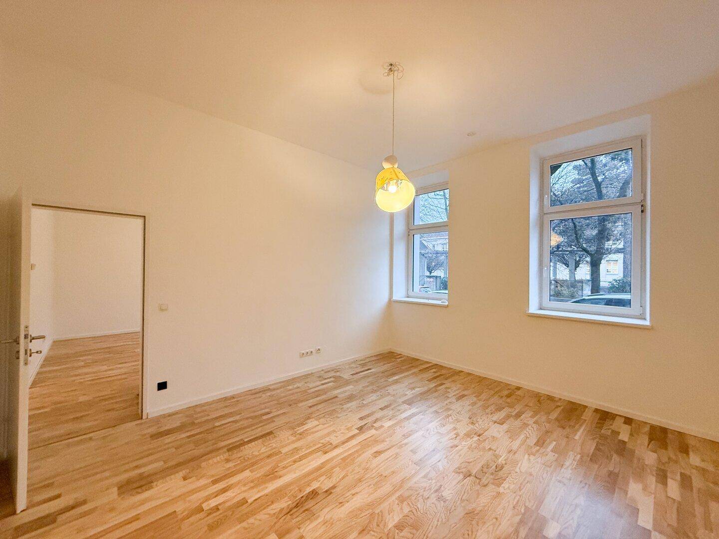 Helles Wohnzimmer mit Parkettboden und zwei Fenstern, bereit zur individuellen Gestaltung.