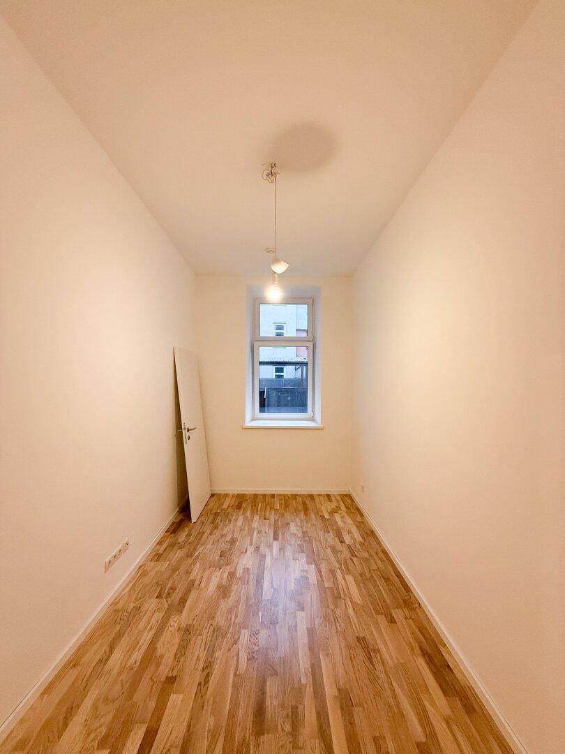 Schmaler Raum mit Holzboden und einem Fenster, ideal als Schlaf- oder Arbeitszimmer.