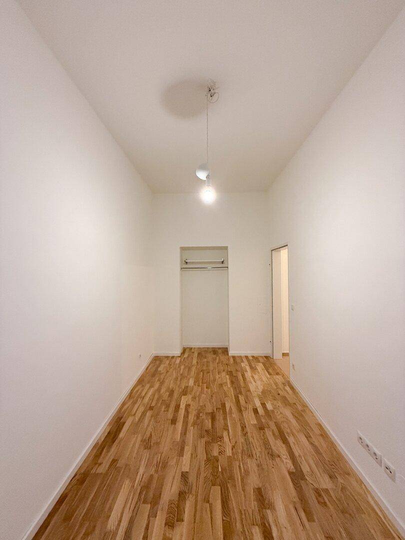 Langer Raum mit Parkettboden und einer offenen Nische für einen Einbauschrank.