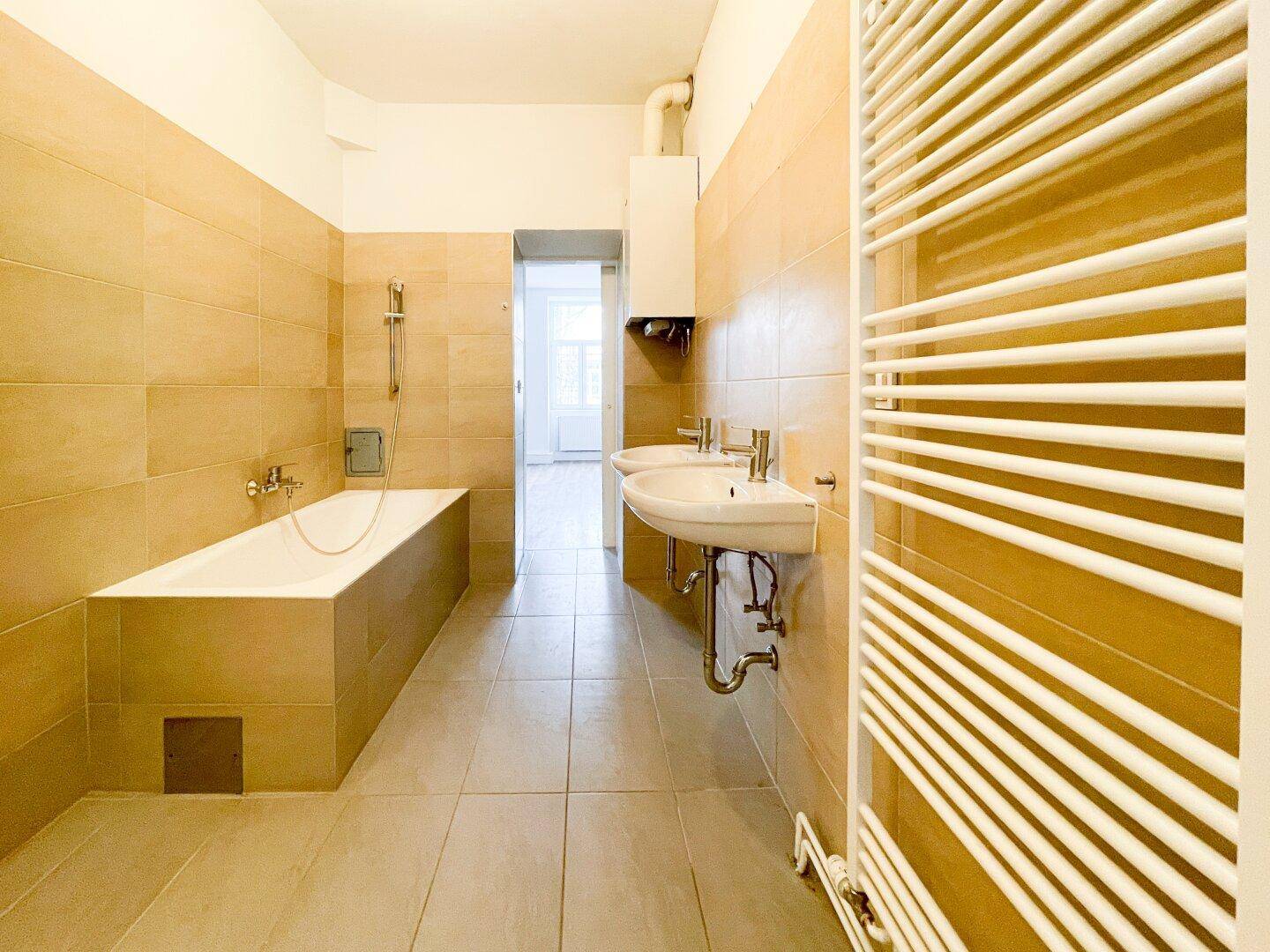 Helles Badezimmer mit Badewanne, zwei Waschbecken und praktischem Handtuchheizkörper.