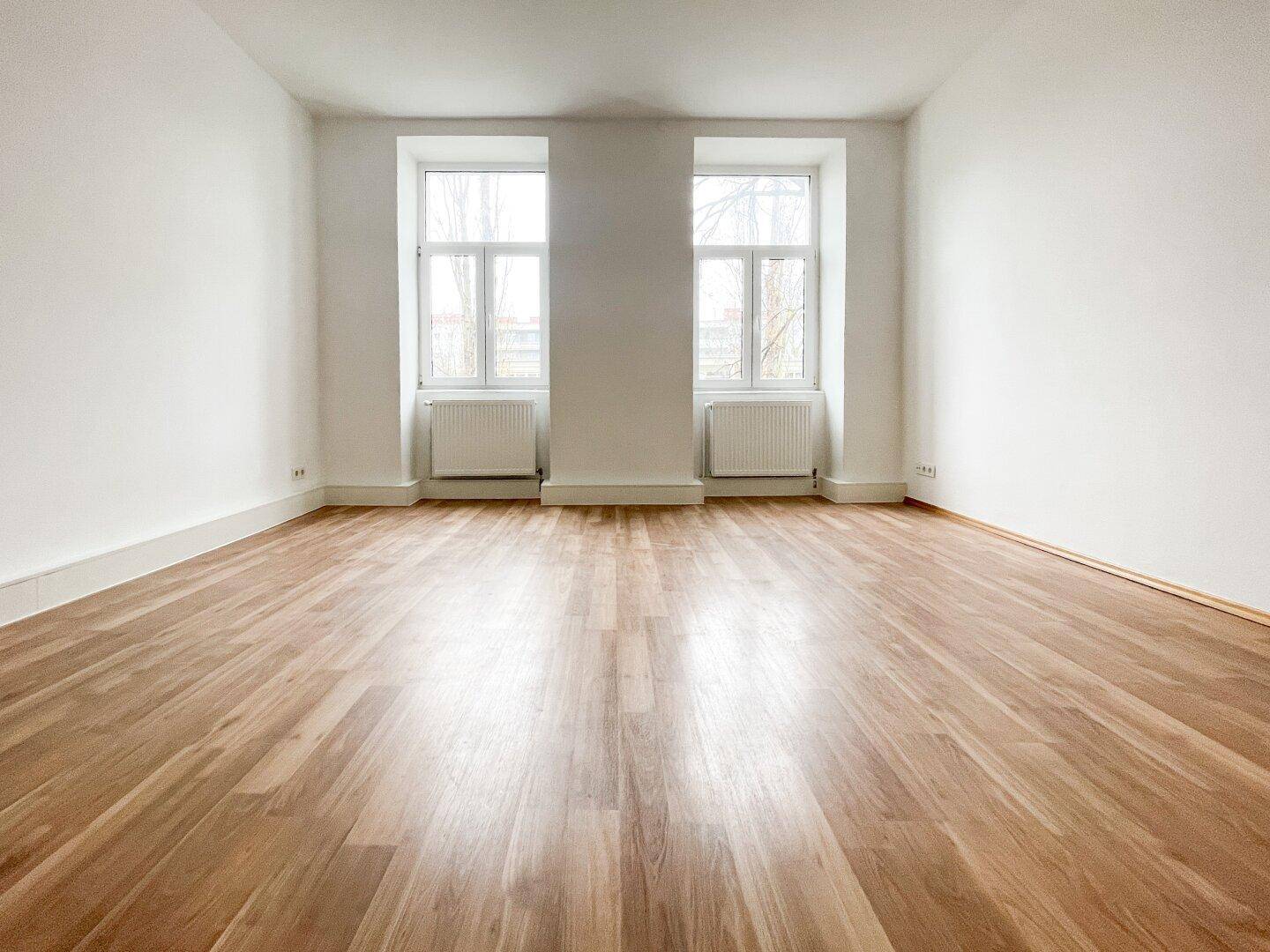 Heller Raum mit Holzboden und zwei Fenstern, ideal als Wohn- oder Schlafzimmer nutzbar.